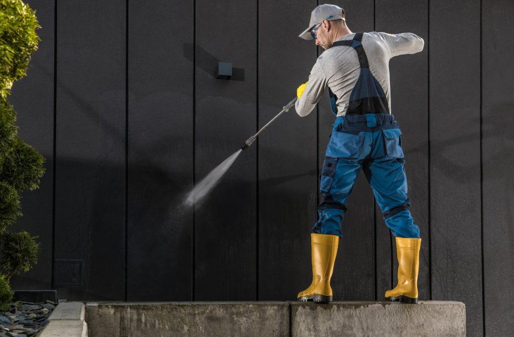 Technician using equipment for safe pressure washing services on a house exterior wall.